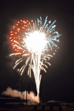Digital painting of multicolor fireworks exploding against the black night sky.